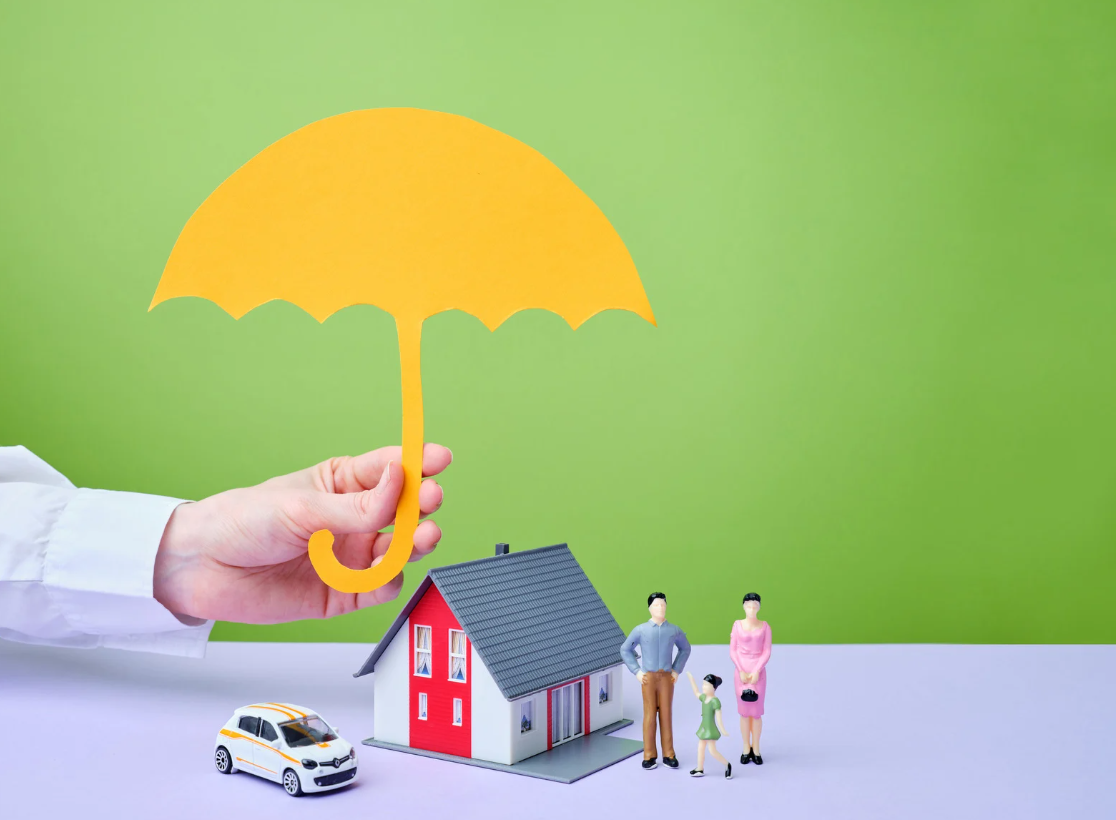 Hand holding paper umbrella over toy house and family representing insurance protection