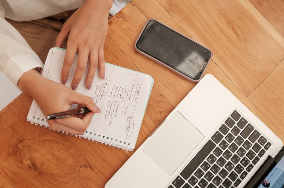 Writing in a notebook in front of laptop